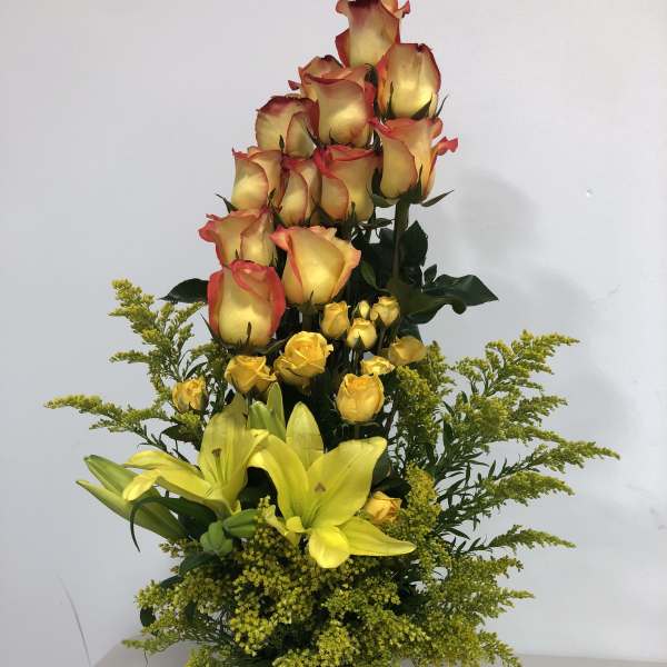 Tall arrangement of yellow lilies and yellow-red roses in a square vase