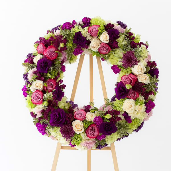 Circular floral wreath on a wooden easel with pink, purple, and cream blooms