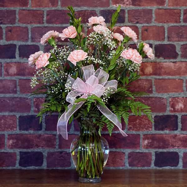 Pink carnations in a clear glass vase with a pink ribbon bow