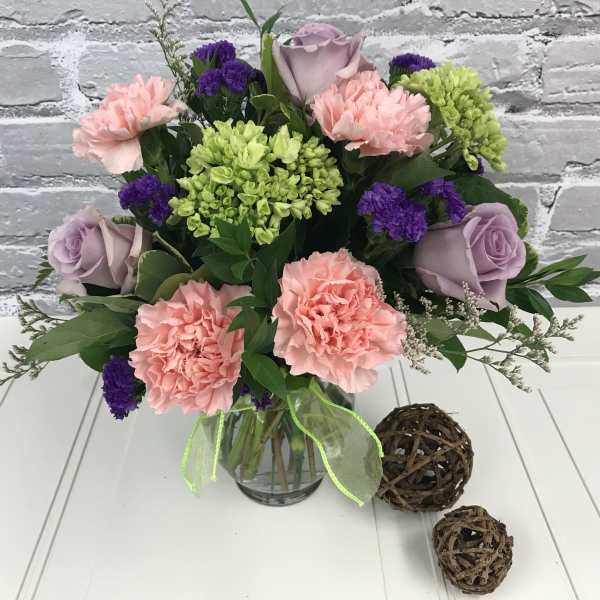 Bouquet of pink carnations, lavender roses, and green hydrangeas in a glass vase