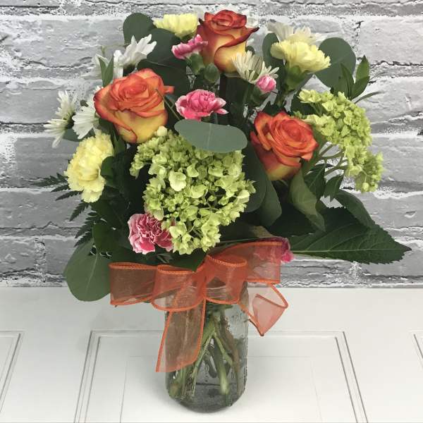 Bouquet of orange roses, pink carnations, and yellow blooms in a glass vase