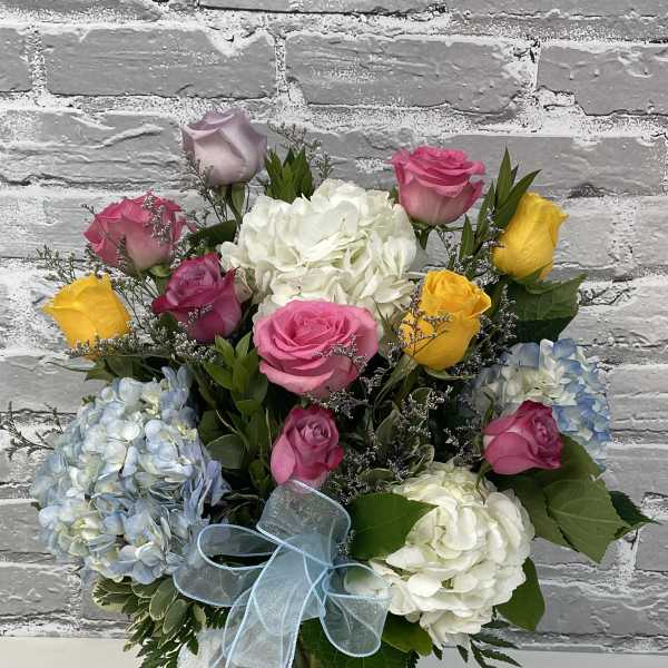 Bouquet of roses and hydrangeas in a glass vase with a blue ribbon