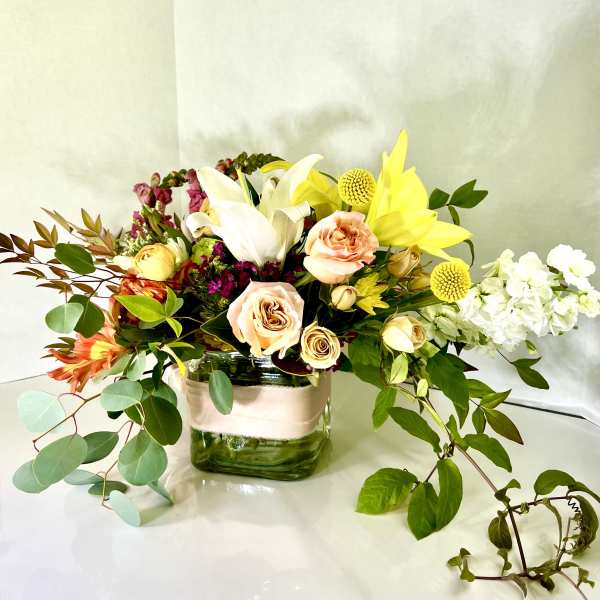 Mixed bouquet in a square glass vase with white lilies and yellow blooms