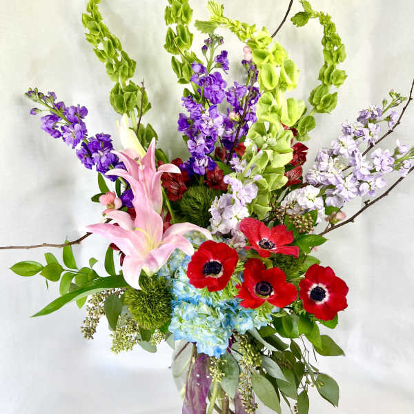 Tall bouquet of pink lilies, red anemones, and purple blooms in a glass vase