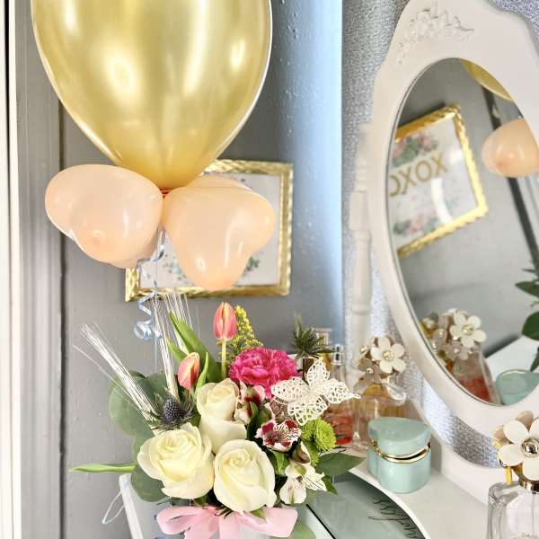 Bouquet of cream and pink flowers in a white vase with gold and peach balloons