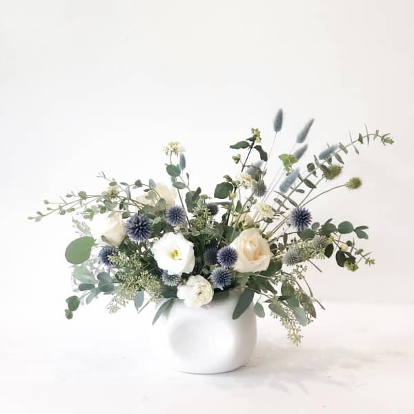 White and cream flowers in a round white vase with blue thistle-like blooms