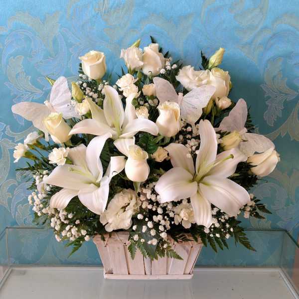 White lilies and roses arranged in a wooden basket with butterfly accents
