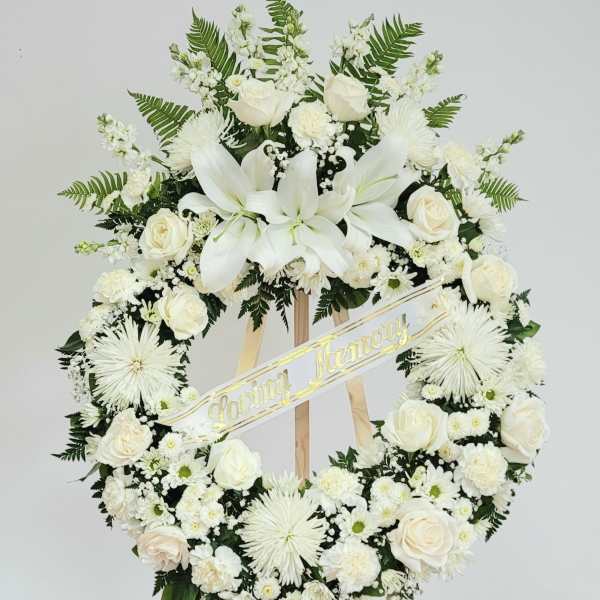 White funeral wreath with roses and lilies on a wooden easel