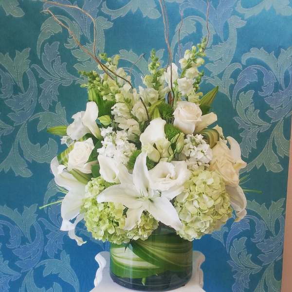 White floral arrangement in a glass vase with lilies, roses, and hydrangeas
