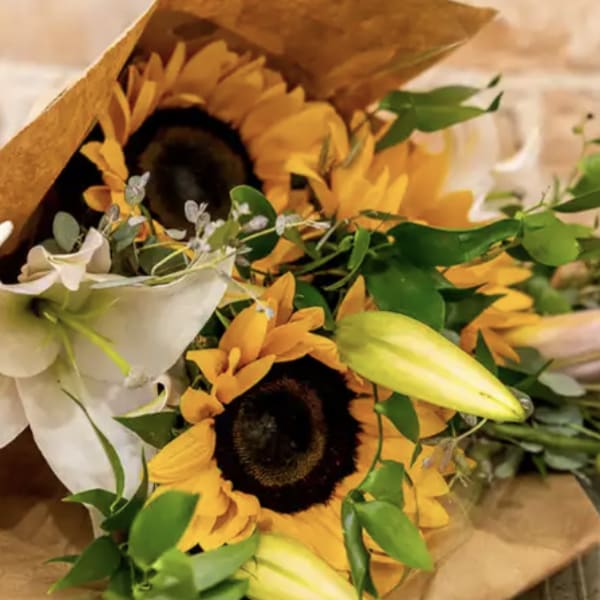 Bouquet with sunflowers, white lilies, and unopened lily buds in brown paper