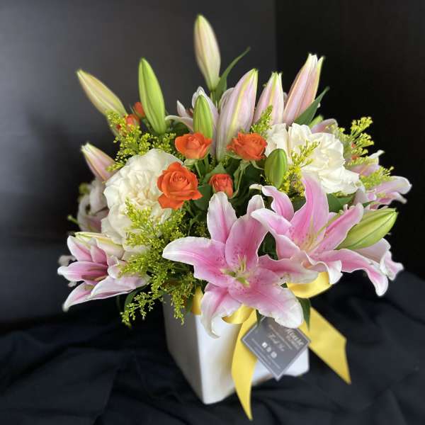 Pink lilies and white roses in a white vase with a yellow ribbon