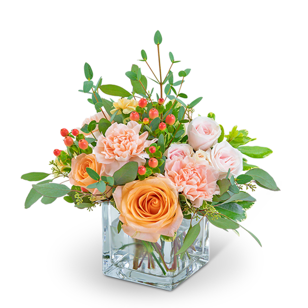 Peach and blush roses with carnations in a clear square vase
