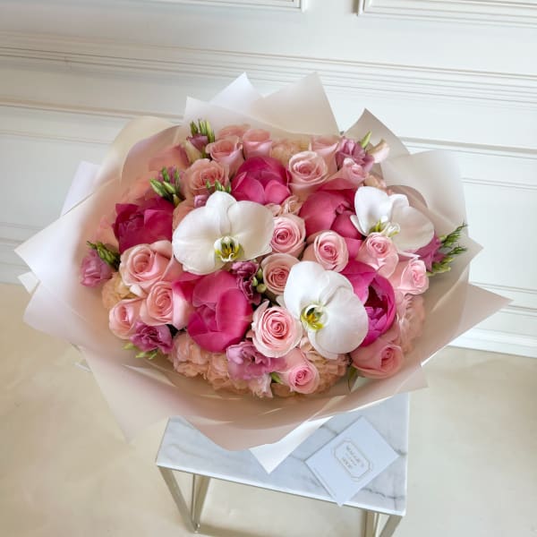 Pink rose bouquet with white orchids wrapped in pale paper