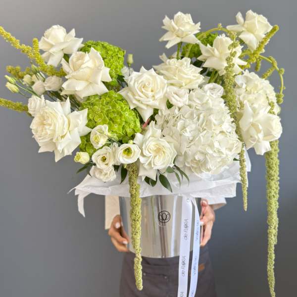 Large arrangement of white roses and hydrangeas with green accents in a silver hatbox container.