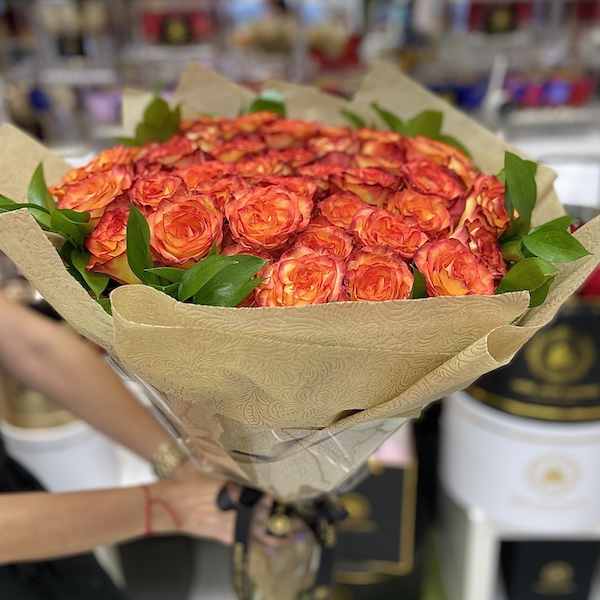 Large bouquet of orange and red roses wrapped in patterned brown paper and cellophane