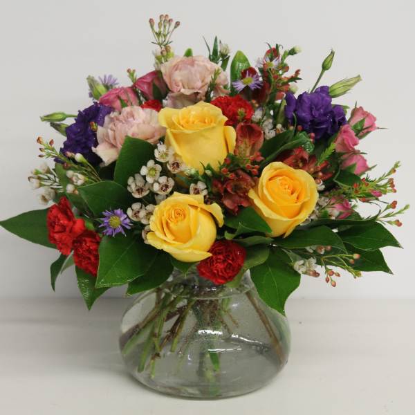 Mixed bouquet of yellow, pink, red, and purple flowers in a glass vase