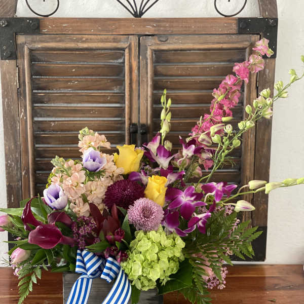 Colorful mixed flower arrangement in a wooden box with a striped ribbon
