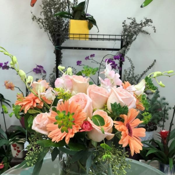 Peach roses and orange daisies in a clear glass vase