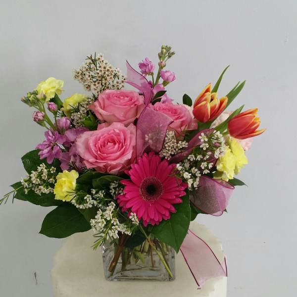 Mixed bouquet of pink roses, gerbera daisies, and tulips in a glass vase