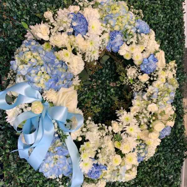 Heart-shaped floral wreath with blue and white flowers and a light blue ribbon
