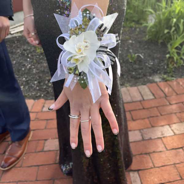 White orchid wrist corsage with white ribbons worn on an arm in a dark sequined dress.