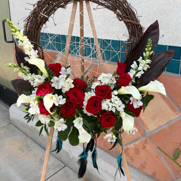 Floral wreath with red roses, white calla lilies, and white blossoms on an easel