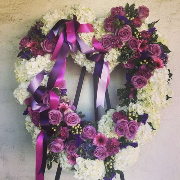 Heart-shaped floral wreath with purple roses and white blooms, tied with magenta ribbons