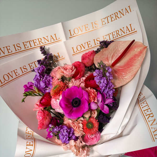 Pink and purple mixed bouquet wrapped in paper with "LOVE IS ETERNAL" text