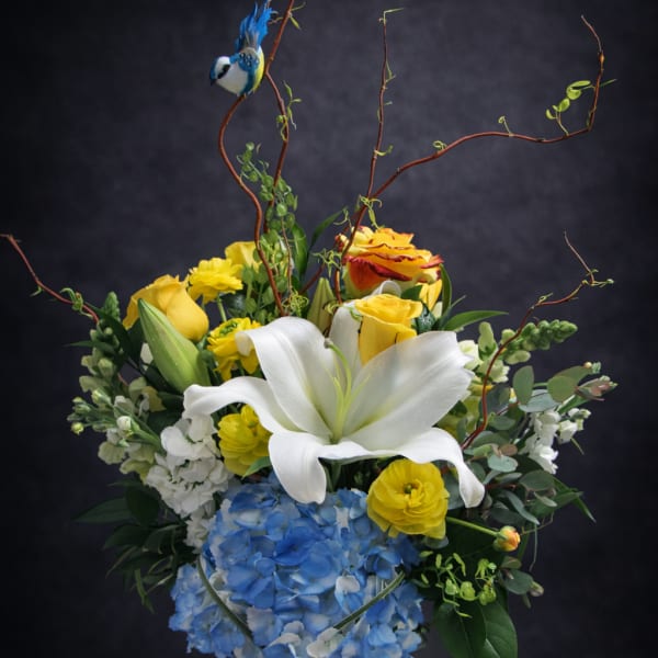 Bouquet of white lilies, yellow roses, and blue hydrangea in a glass vase