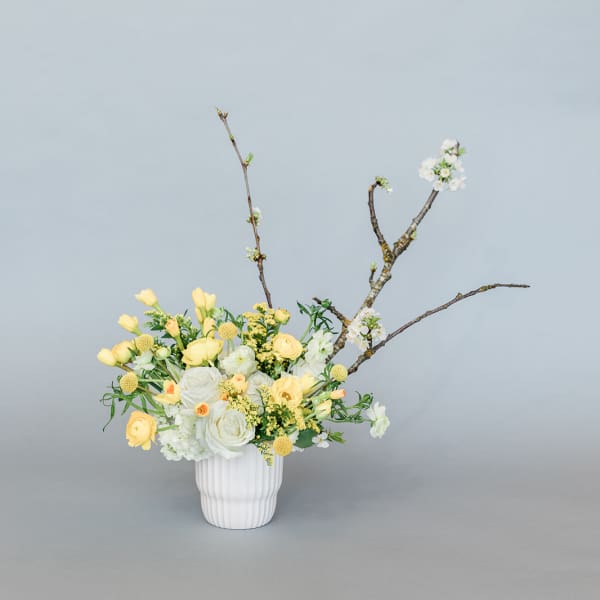 Yellow and white floral arrangement in a white vase with branching stems