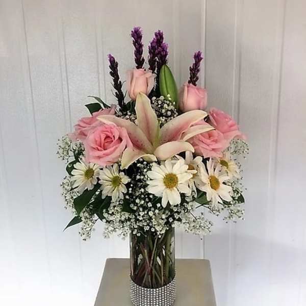 Pink roses and lilies arranged in a glass vase with white daisies