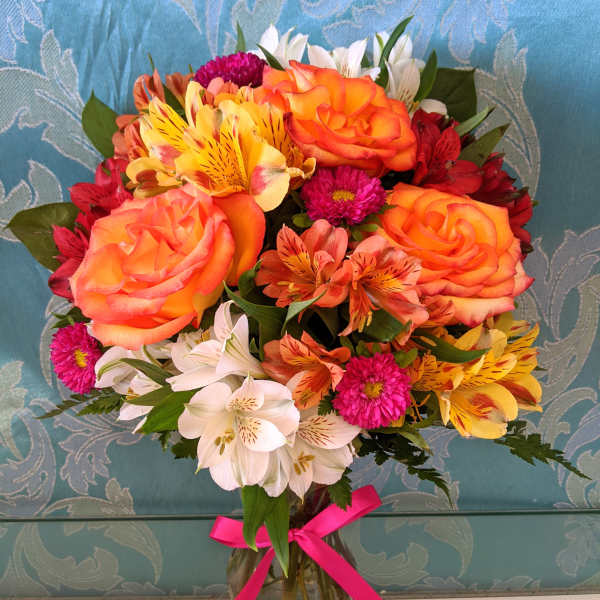 Mixed bouquet of orange roses, white lilies, and pink flowers in a glass vase