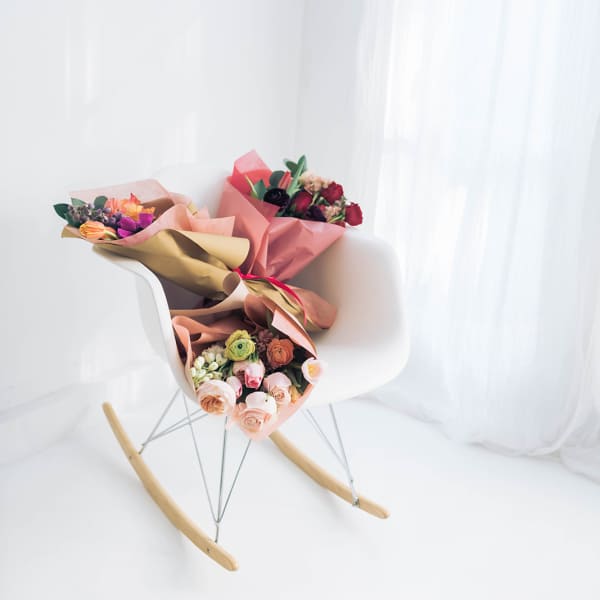 Two wrapped bouquets on a white chair by a bright window.