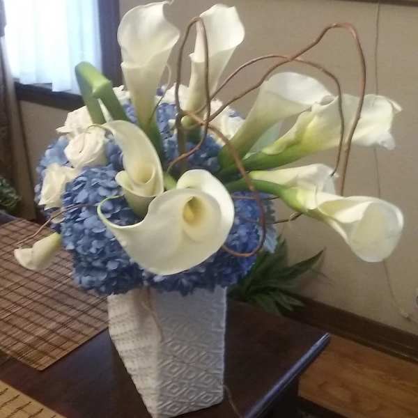 White calla lilies arranged with blue hydrangeas in a tall white vase