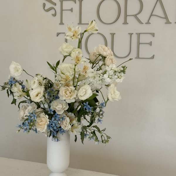 Tall white floral arrangement in a white vase with blue accents