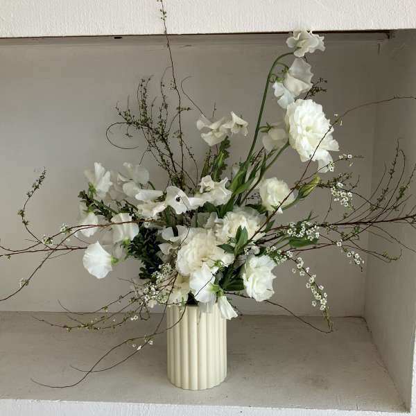 White floral arrangement in a ribbed cream vase