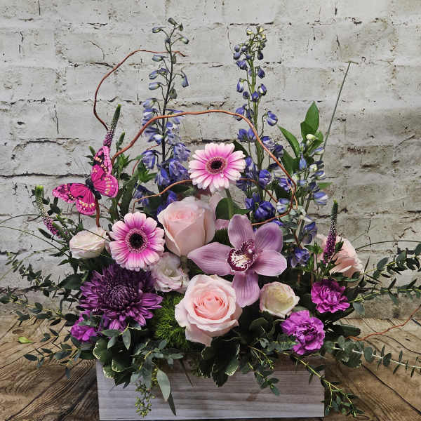 Pink and purple floral arrangement in a white wooden box with a butterfly accent