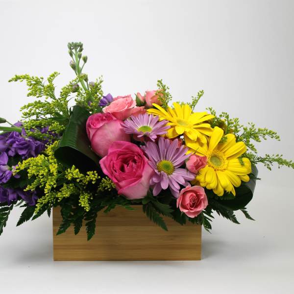 Mixed bouquet of pink roses, yellow daisies, and purple flowers in a wooden box