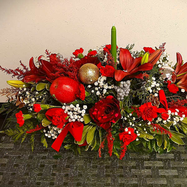Low floral centerpiece with red lilies, roses, ornaments, and a green taper candle