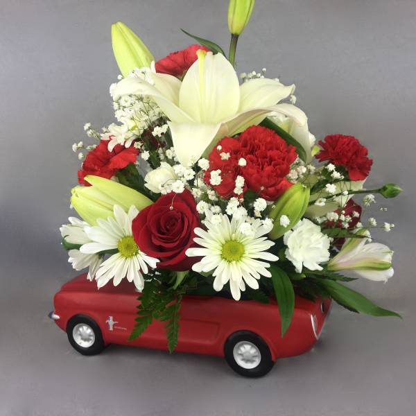 Red and white flower arrangement in a red toy car container