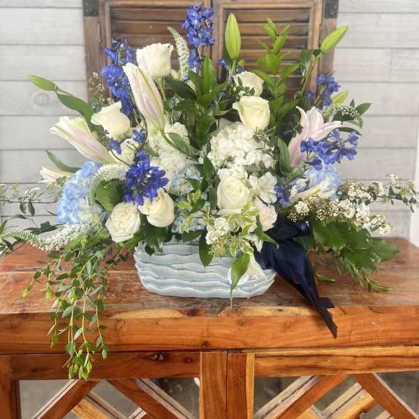 Blue and white floral arrangement in a ceramic vase with trailing greenery