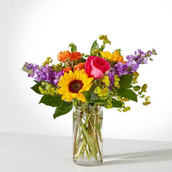 Mixed bouquet with a sunflower, roses, and purple flowers in a glass vase