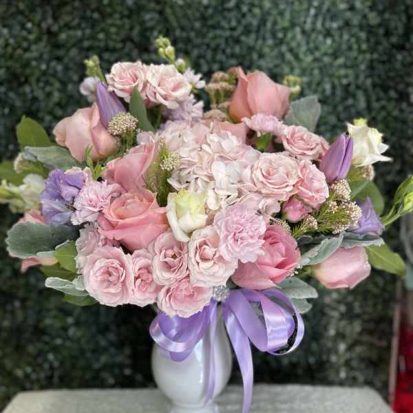 Pink and lavender bouquet in a white vase with a purple ribbon