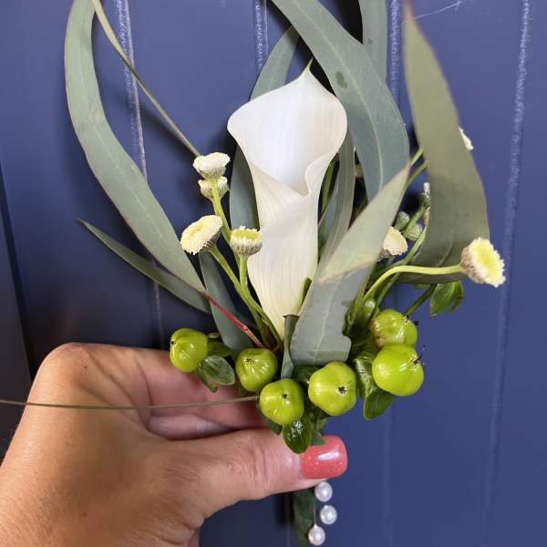 White calla lily with small white blooms and green berries in a hand-held piece