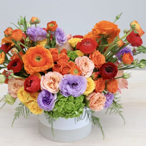 Colorful bouquet of ranunculus, roses, and lisianthus in a round box