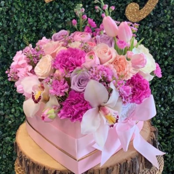 Pink and lavender floral arrangement in a pink box with a ribbon