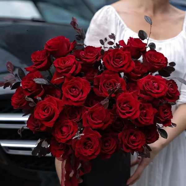 Bouquet of red roses in a black box with dark foliage