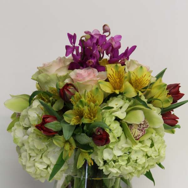 Mixed arrangement of green hydrangeas, pink roses, orchids and tulips in a clear glass vase