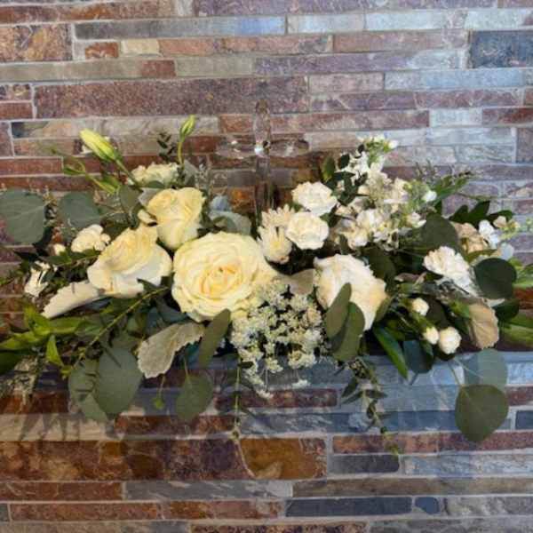 White rose arrangement with greenery against a brick wall