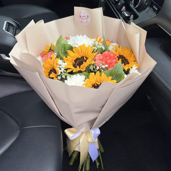 Bouquet of sunflowers, white chrysanthemums, and pink carnations wrapped in beige paper